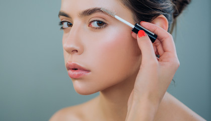 Care beauty eyebrow. Beautiful woman with brow brush in hand. Attractive sexy girl with glamorous professional nude makeup brushing up her perfect eyebrows with brush. Natural eyebrow makeup look.