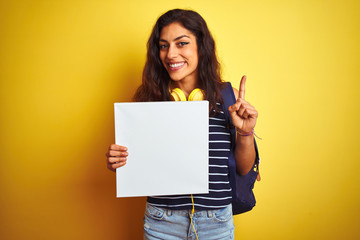 Fototapeta na wymiar Young beautiful student woman holding banner standing over isolated yellow background surprised with an idea or question pointing finger with happy face, number one