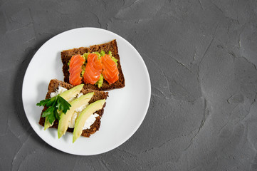 Two toast with avocado slice with cream cheese and smash avocado with red fish salmon on white plate and concrete top view
