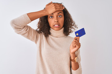 Young brazilian woman holding credit card standing over isolated white background stressed with...