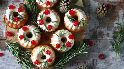 Fototapeta na wymiar Christmas muffins with rosemary, white icing and red berries. Elegant holiday cakes. Christmas composition. Selective focus. Macro.