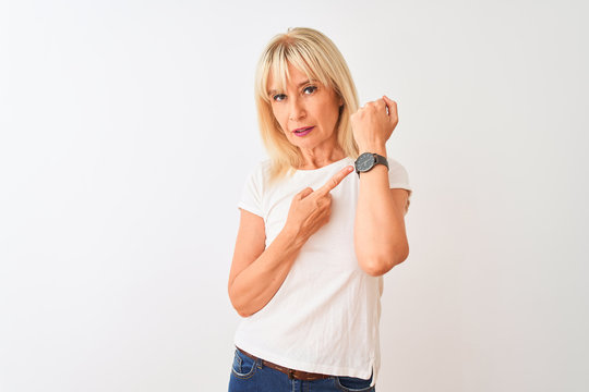 Middle age woman wearing casual t-shirt standing over isolated white background In hurry pointing to watch time, impatience, looking at the camera with relaxed expression