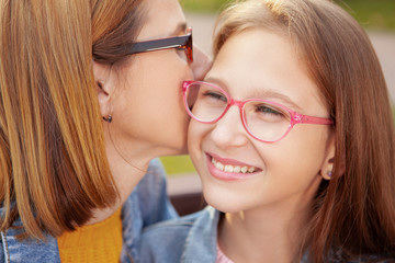 Close up of a lovely young girl smiling joyfully as her mother kissing her on the cheek. Mom and...