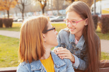 Happy mother and daughter smiling at each other, enjoying warm autumn outdoors at city park