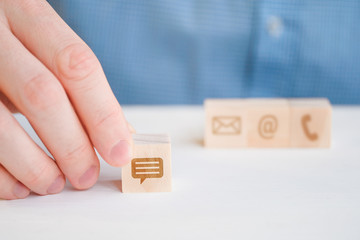 A man in a shirt holds with his hand an abstract icon on a wooden message cube against the background of an envelope, internet and phone. Feedback concept.