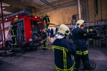 Firefighters preparing their uniform and the firetruck in the background inside the fire station