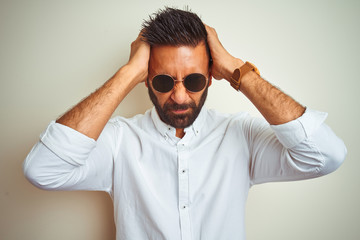 Obraz premium Handsome indian buinessman wearing shirt and sunglasses over isolated white background suffering from headache desperate and stressed because pain and migraine. Hands on head.