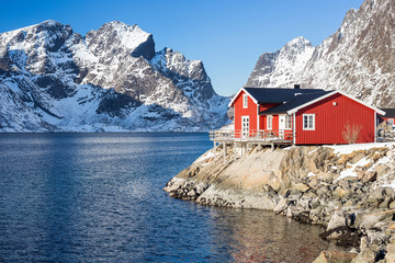 Red Fisherman house in front of a snow covered mountain range on Lofoten islands in winter