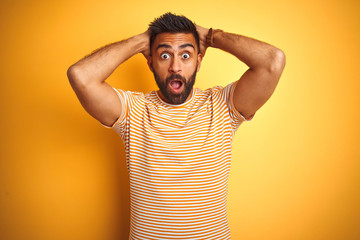 Young indian man wearing t-shirt standing over isolated yellow background Crazy and scared with...
