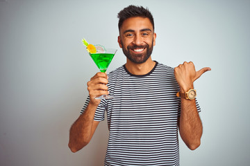 Young indian man drinking cocktail with alcohol standing over isolated white background pointing and showing with thumb up to the side with happy face smiling