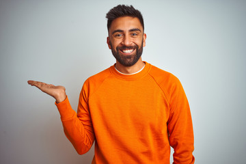 Young indian man wearing orange sweater over isolated white background smiling cheerful presenting...