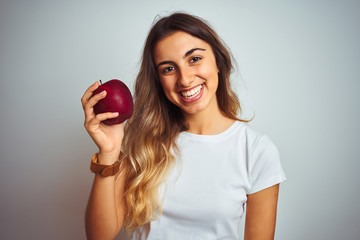 Young beautiful woman eating red apple over grey isolated background with a happy face standing and smiling with a confident smile showing teeth