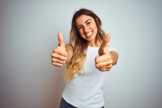 Young beautiful woman wearing casual white t-shirt over isolated background success sign doing positive gesture with hand, thumbs up smiling and happy. Cheerful expression and winner gesture.