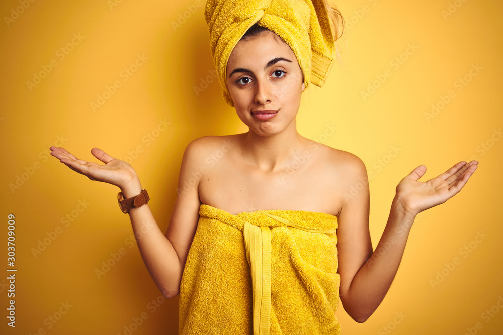 Canvas Prints Young beautiful woman wearing a shower towel after bath over yellow isolated background clueless and confused expression with arms and hands raised. Doubt concept.