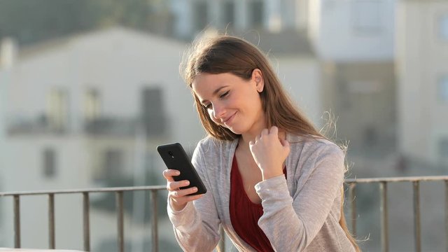 Happy woman using mobile phone in a balcony with copy space at side in a sunny 
