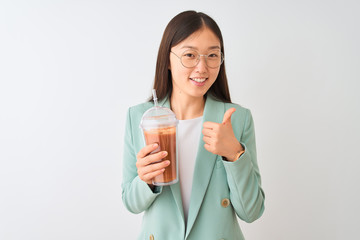 Young chinese woman drinking tomato smoothie over isolated white background happy with big smile doing ok sign, thumb up with fingers, excellent sign