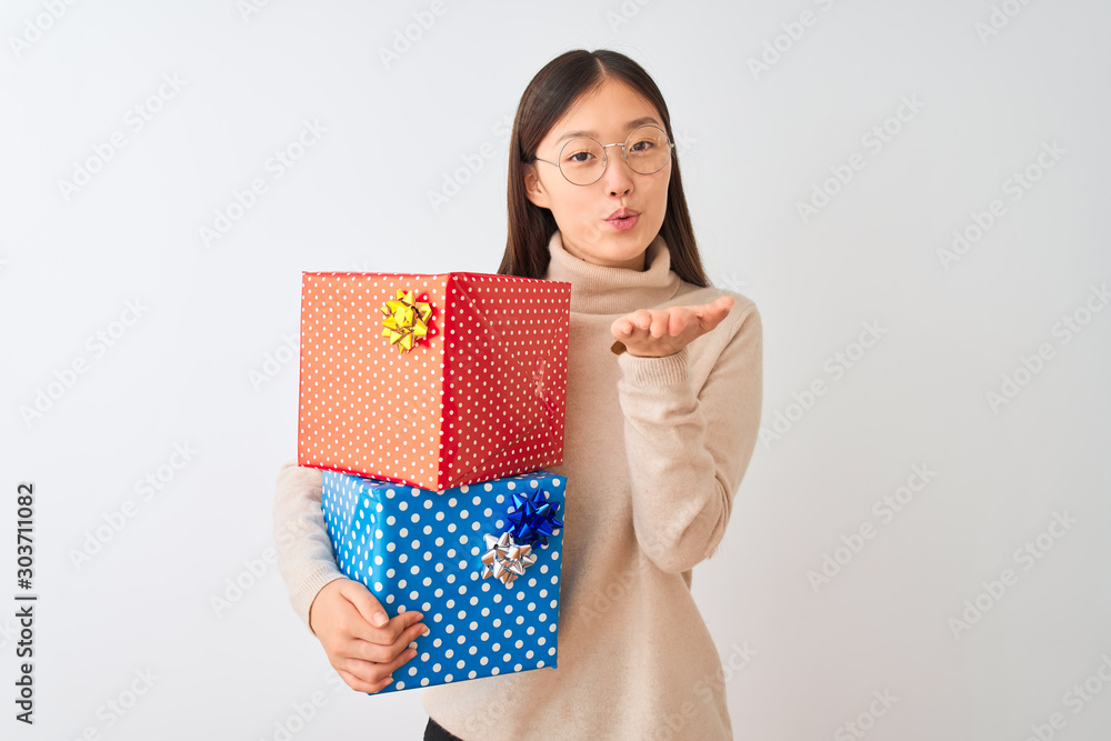 Sticker Young chinese woman holding birthday gifts over isolated white background looking at the camera blowing a kiss with hand on air being lovely and sexy. Love expression.