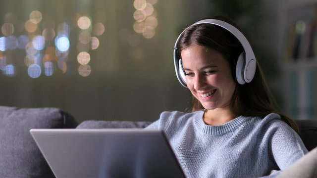 Happy woman with headphones checking laptop sitting on a couch at home in the 