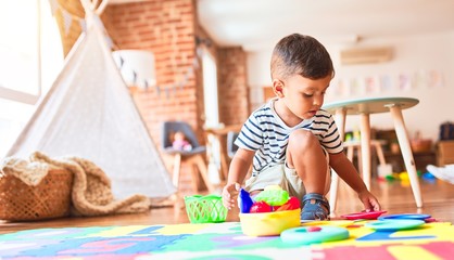 Beautiful toddler boy sitting on puzzle playing meals with plastic plates, fruits and vegetables at...