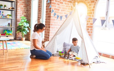 Beautiful teacher and toddler boy sitting on the floor playing inside  tipi at kindergarten
