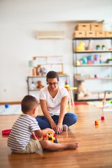 Fototapeta premium Beautiful teacher and toddler boy playing with tractor and cars at kindergarten