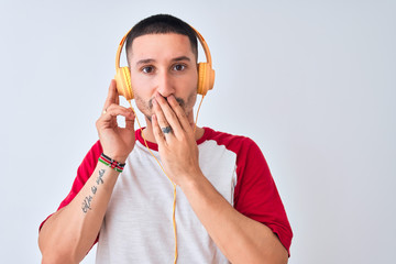 Young handsome man wearing headphones over isolated background cover mouth with hand shocked with...