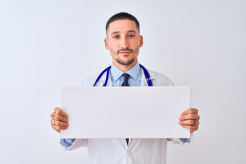 Young doctor man holding blank advertising banner over isolated background with a confident expression on smart face thinking serious