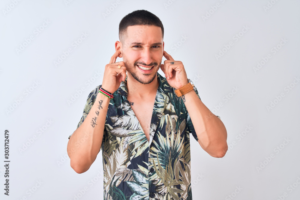 Wall mural Young handsome man wearing Hawaiian summer shirt over isolated background covering ears with fingers with annoyed expression for the noise of loud music. Deaf concept.