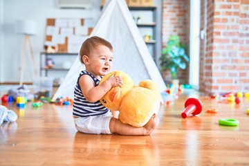 Fototapeta premium Adorable toddler smiling happy playing around lots of toys at kindergarten