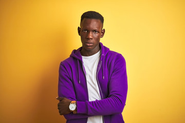Obraz premium African american man wearing purple sweatshirt standing over isolated yellow background skeptic and nervous, disapproving expression on face with crossed arms. Negative person.
