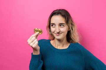 Woman holding a physical bitcoin cryptocurrency in her hand. Thinking about question, pensive expression, looks incredulous. Change in the growth and fall of cryptocurrency.	