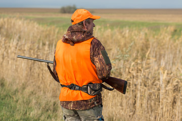 A man with a gun in his hands and an orange vest on a pheasant hunt in a wooded area in cloudy...