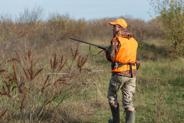 Hunting period, autumn season open. A hunter with a gun in his hands in hunting clothes in the autumn forest in search of a trophy. A man stands with weapons and hunting dogs tracking down the game.	