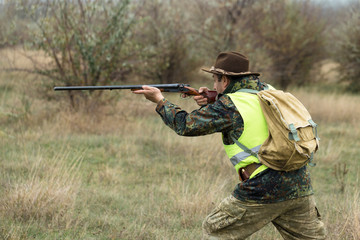 Hunting period, autumn season open. A hunter with a gun in his hands in hunting clothes in the autumn forest in search of a trophy. A man stands with weapons and hunting dogs tracking down the game.	