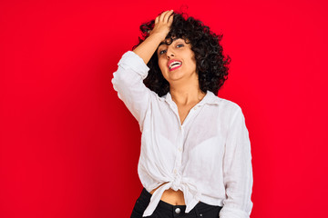 Young arab woman with curly hair wearing white casual shirt over isolated red background surprised...