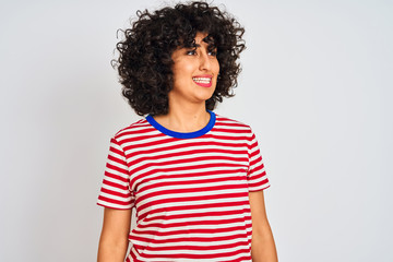 Young arab woman with curly hair wearing striped t-shirt over isolated white background looking away to side with smile on face, natural expression. Laughing confident.