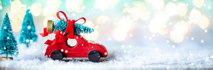 Toy Wooden Car Carrying Christmas Tree Through Snowy Forest With Bright Soft Bokeh Lights Background - Christmas Concept