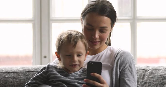 Happy mom teaching kid son laughing using looking at phone