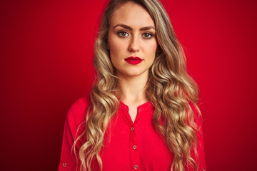 Young beautiful woman standing over red isolated background with a confident expression on smart face thinking serious