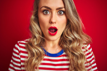 Young beautiful woman wearing stripes t-shirt standing over red isolated background scared in shock with a surprise face, afraid and excited with fear expression