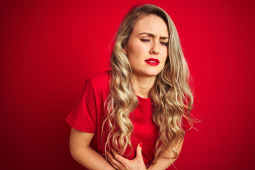 Young beautiful woman wearing basic t-shirt standing over red isolated background with hand on stomach because indigestion, painful illness feeling unwell. Ache concept.