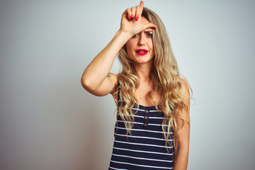 Young beautiful woman wearing stripes t-shirt standing over white isolated background making fun of people with fingers on forehead doing loser gesture mocking and insulting.