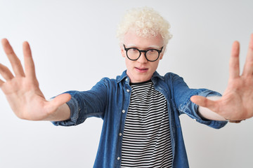 Young albino blond man wearing denim shirt and glasses over isolated white background doing stop gesture with hands palms, angry and frustration expression