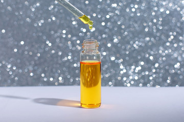 Oily drop falls from cosmetic pipette on light background