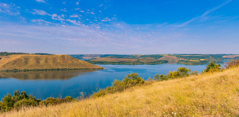 panorama landscape of nature reserve scenic view yellow grass land and hills around smooth lake reservoir in spring time clear weather day 