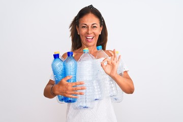 Middle age beautiful woman recycling plastic bottles standing over isolated white background doing ok sign with fingers, excellent symbol