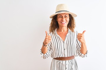 Obraz na płótnie Canvas Middle age businesswoman wearing striped dress and hat over isolated white background success sign doing positive gesture with hand, thumbs up smiling and happy. Cheerful expression and winner gesture