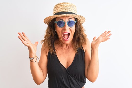 Middle age woman wearing black t-shirt sunglasses and hat over isolated white background very happy and excited, winner expression celebrating victory screaming with big smile and raised hands