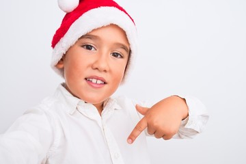Beautiful kid boy wearing Christmas Santa hat make selfie over isolated white background with...