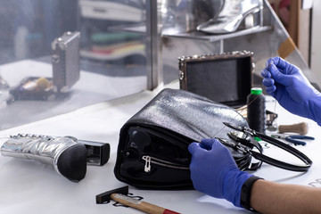 The master repair a leather women's handbag. Close up of master hands, handbag and tools. 